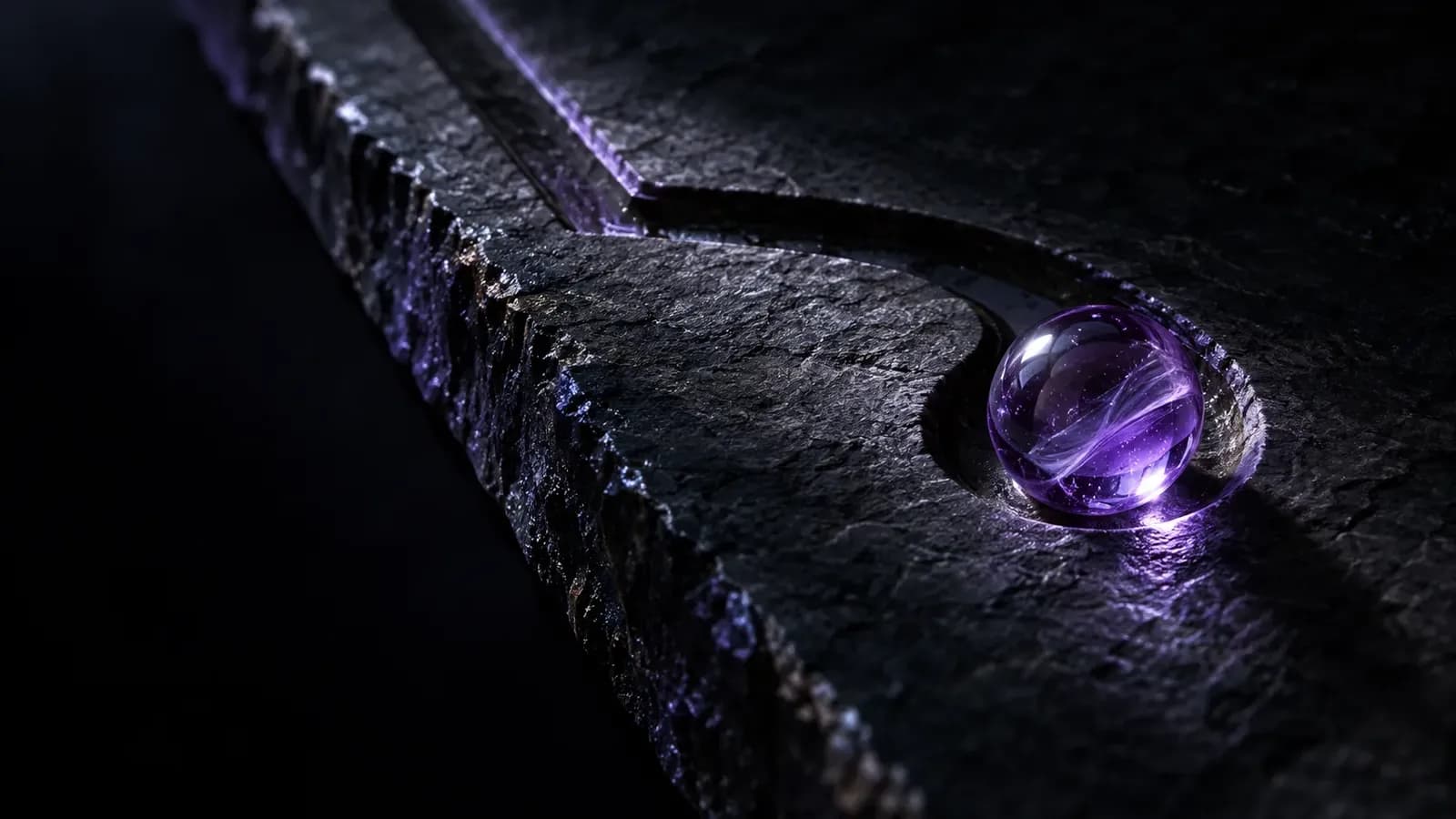 A lilac glass marble resting in a small hollow at the end of a curved channel carved into dark slate, lit by a single narrow beam against a near-black background.
