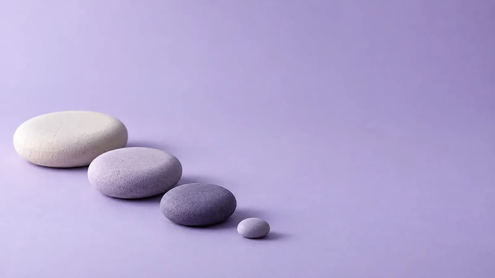 Three smooth ceramic stepping stones in cream, lilac and violet-grey, shrinking in size along a gentle curve on a seamless lavender studio backdrop, with a tiny pebble nearby.
